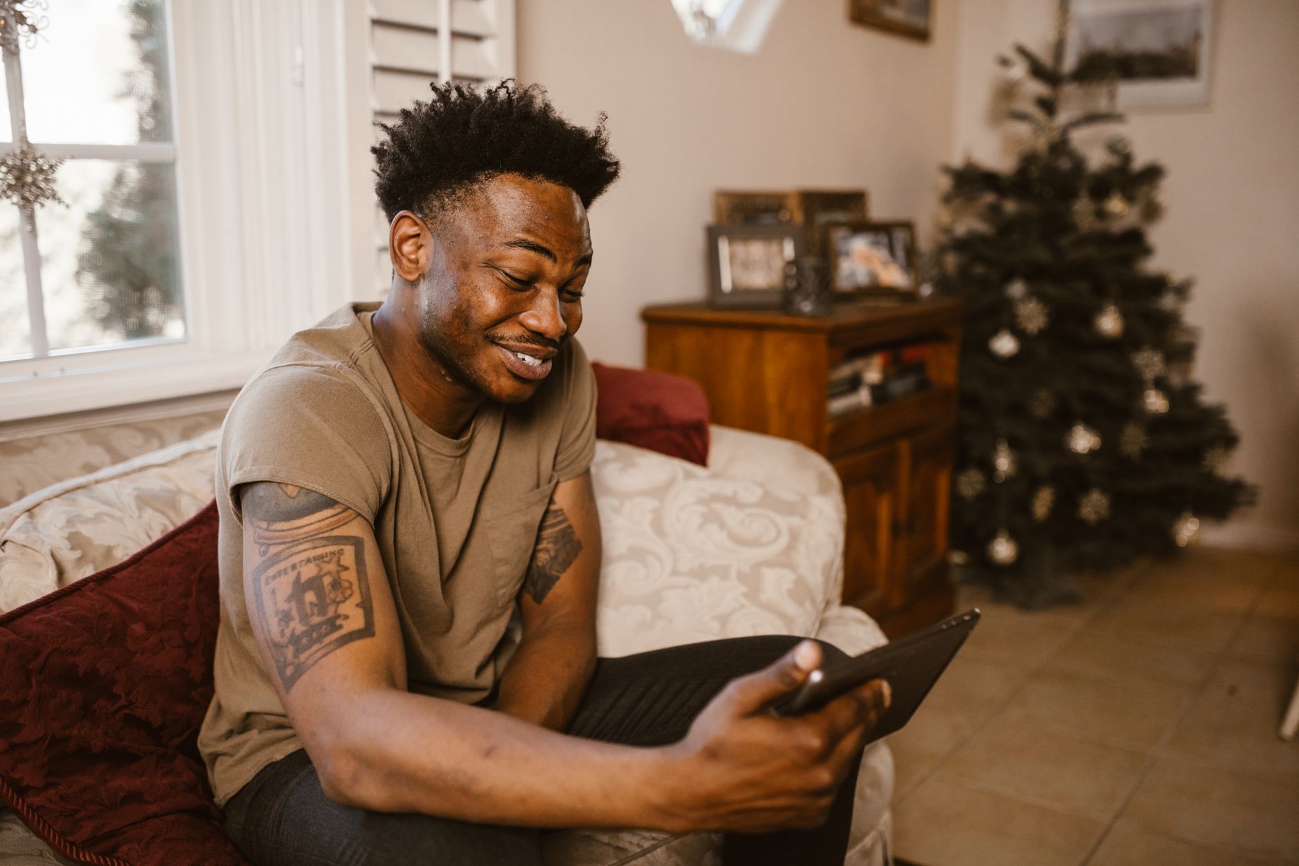Homem sorridente numa videochamada, sentado confortavelmente em casa perto de uma árvore de Natal decorada.