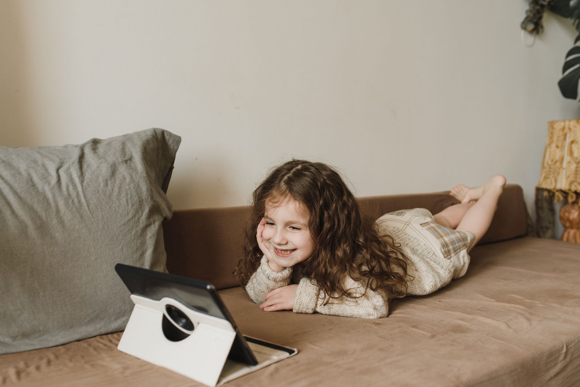 Uma jovem a assistir felizmente a um tablet, deitada num sofá em casa, num ambiente acolhedor.