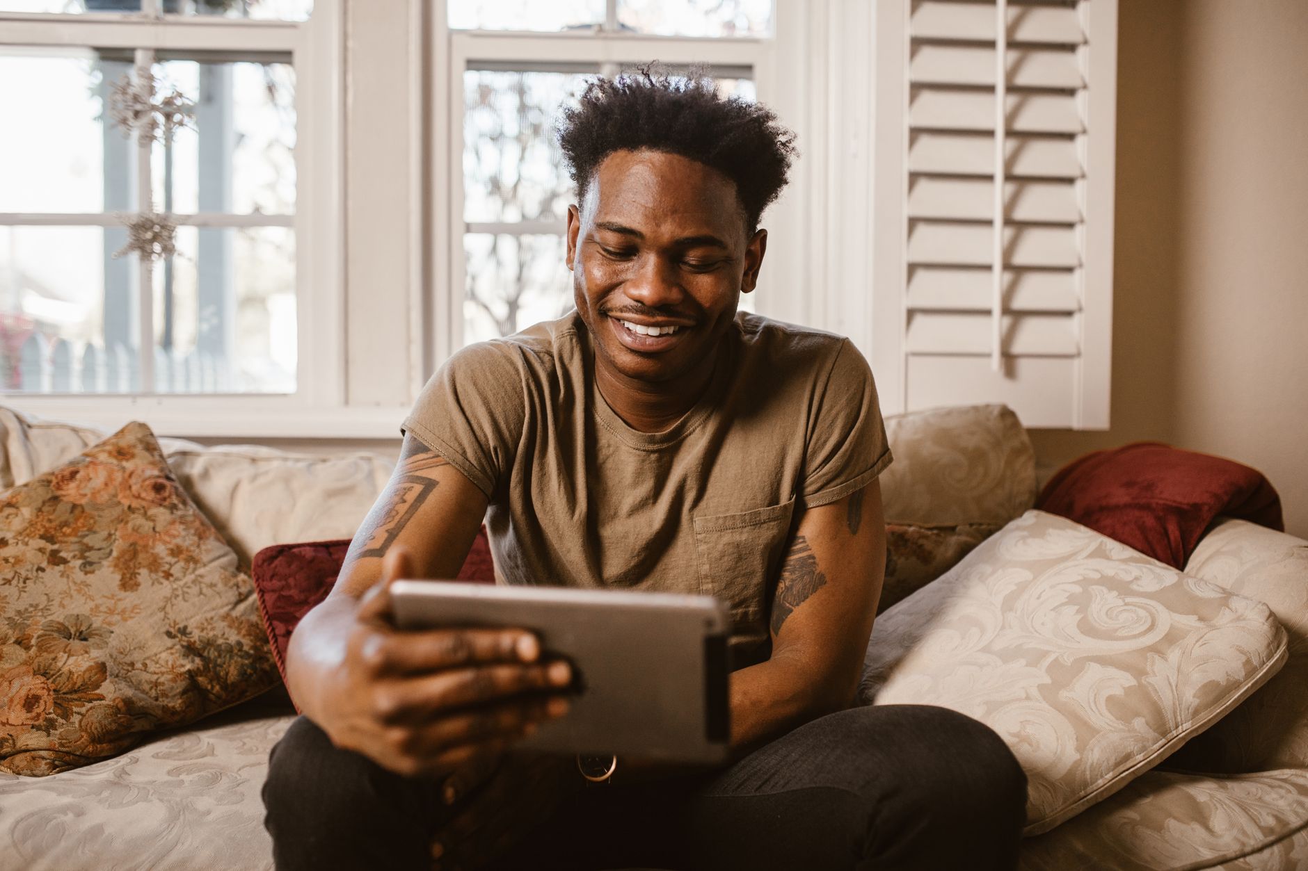 Homem feliz a usar um tablet numa videochamada, sentado confortavelmente no sofá em casa.