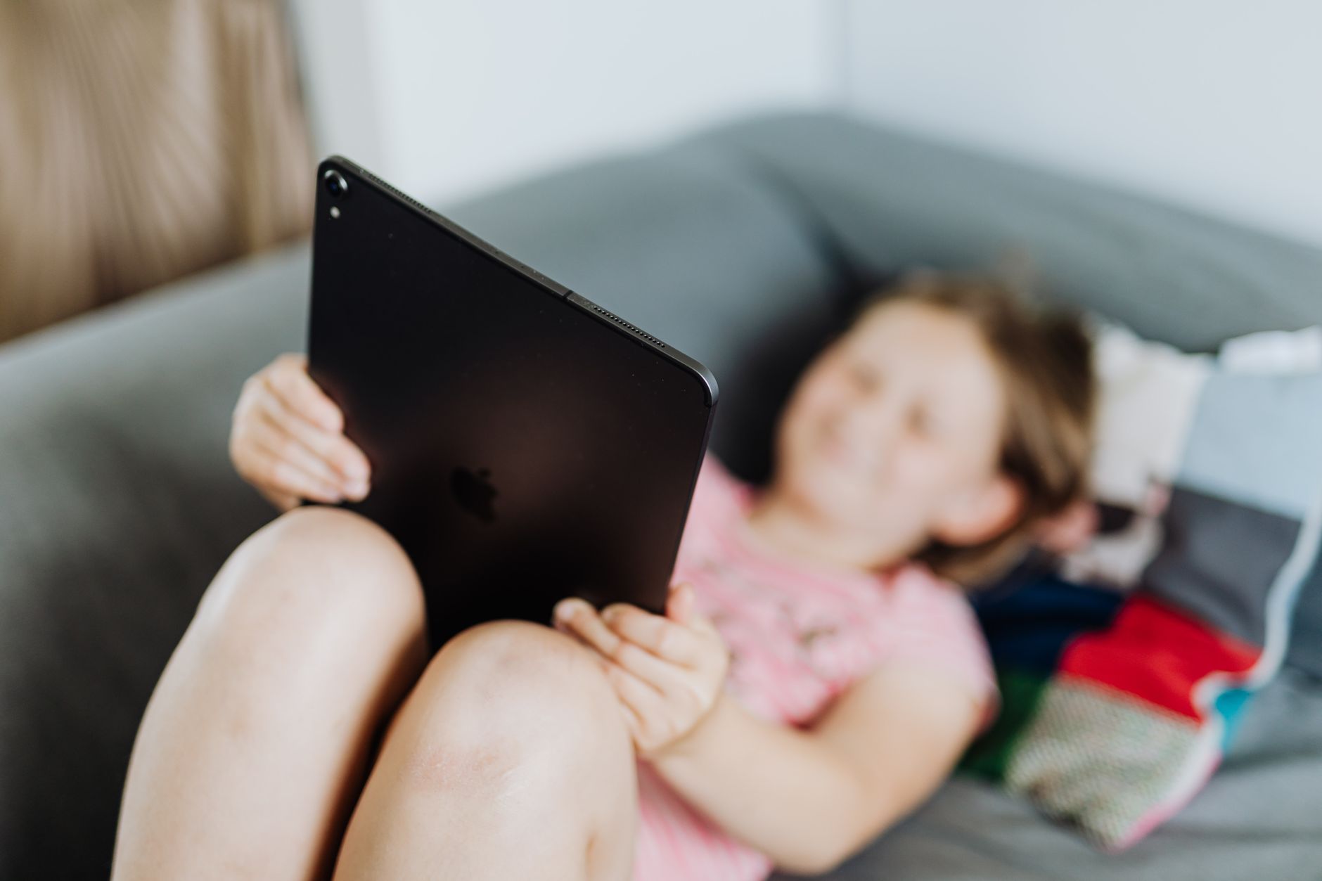 Menina a usar um tablet, relaxada num sofá com fundo desfocado.